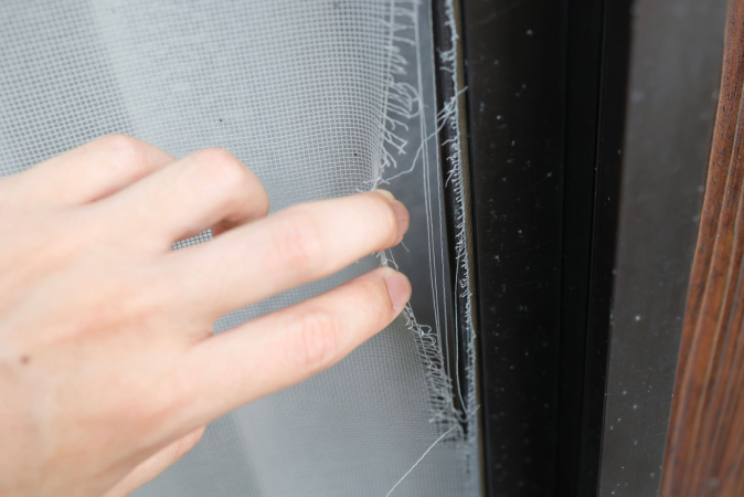 A person pulling back the ripped edges of a screen door
