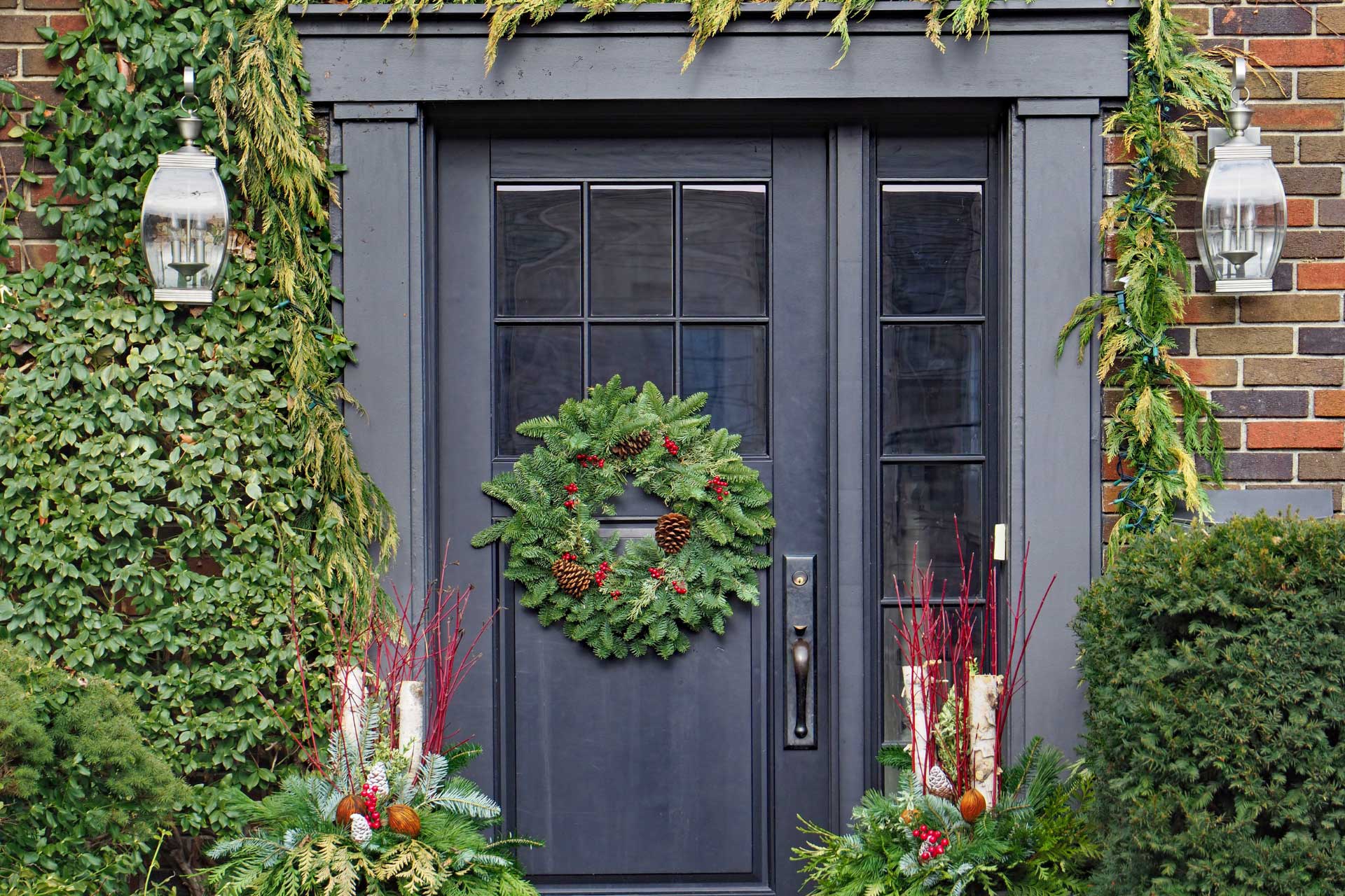 A black front door decorated with greenery, pinecones, and holly