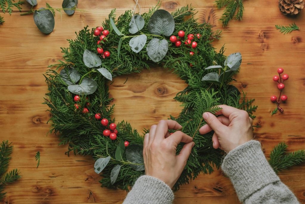 Closeup of someone’s hands making a Christmas wreath to decorate a front door
