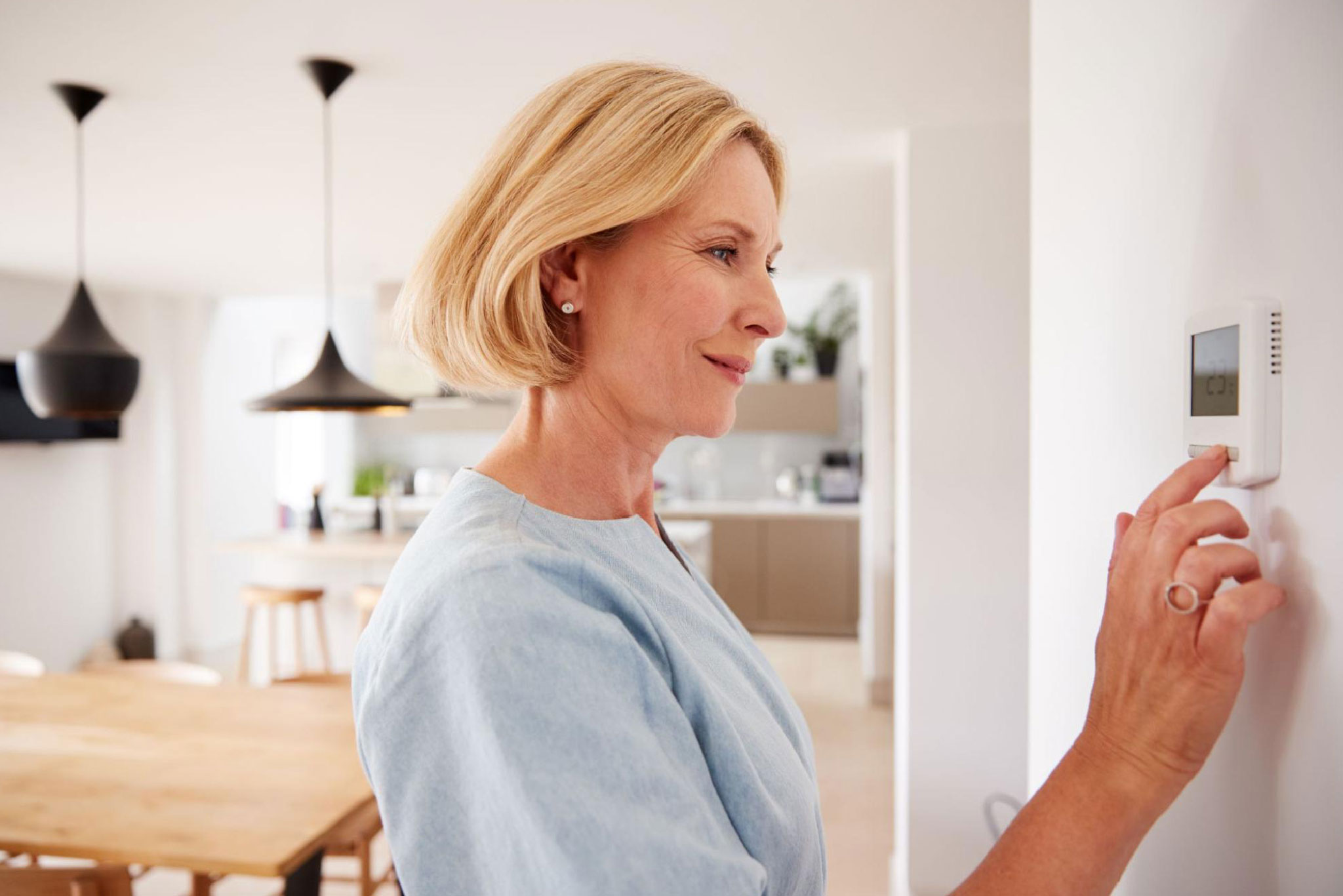 A woman looking at her home’s thermostat happily