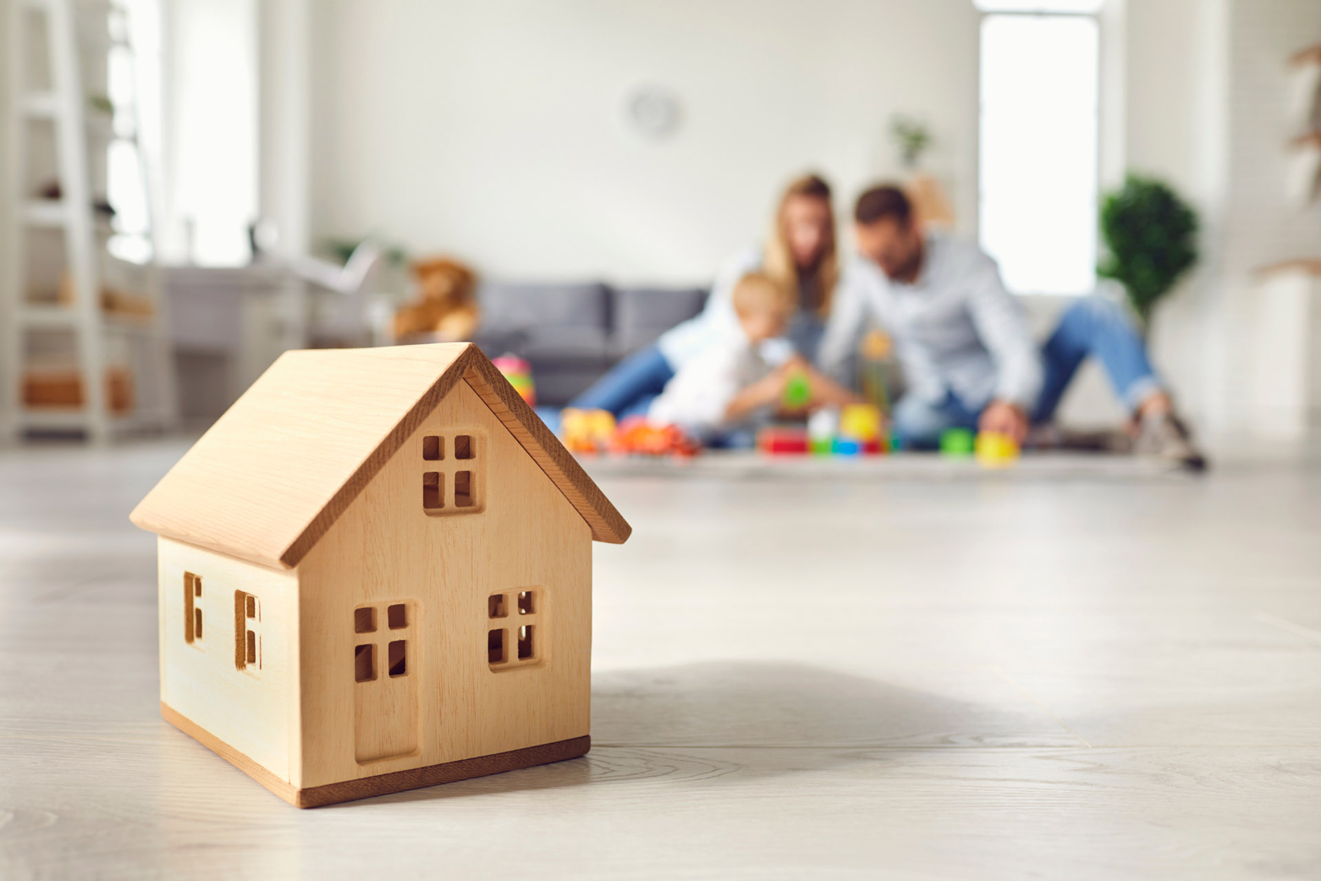 a miniature wooden home with a happy protected family in the background