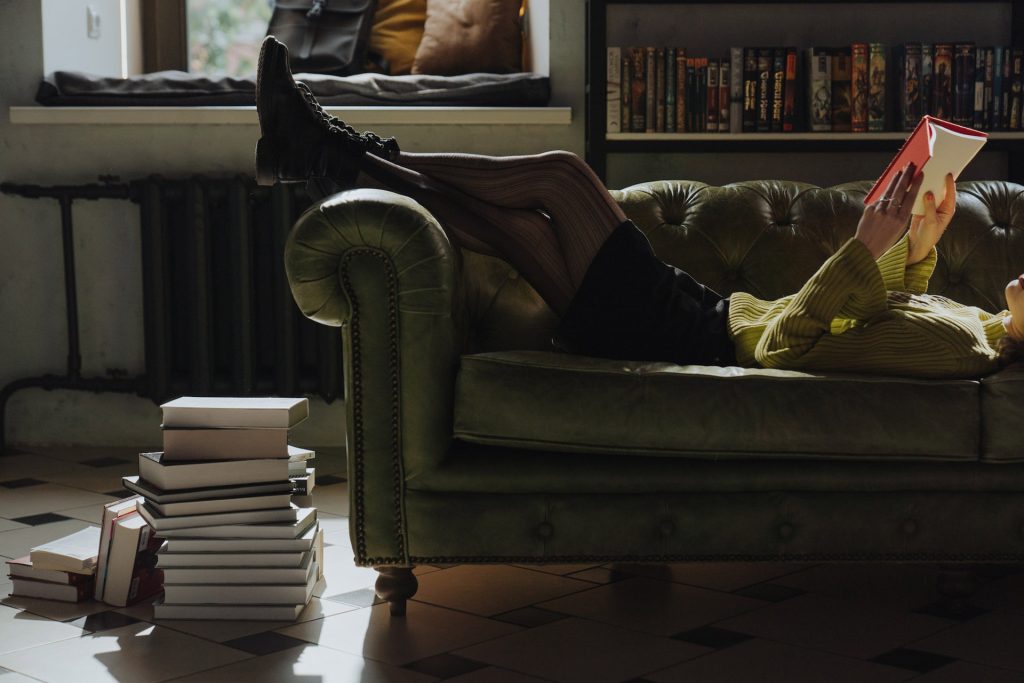 A person reading a book on a couch in a dark room