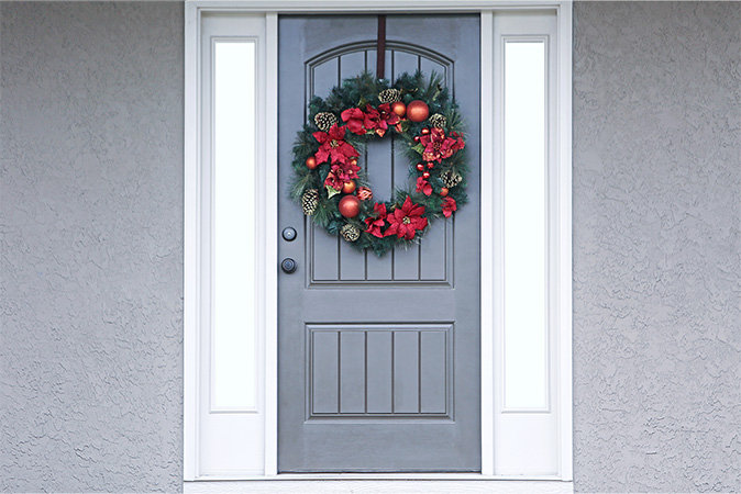 A grey steel entry door with a wreath hung on it
