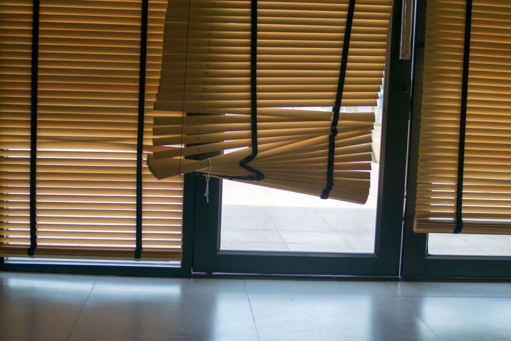 Broken horizontal blinds partially covering a glass door 