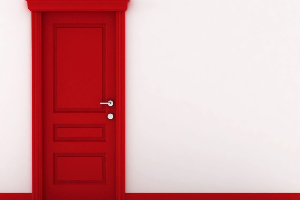 A red door with matching red colonial-style door trim and baseboard trim against a cream wall