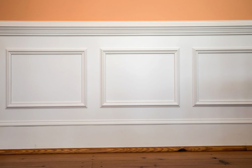 White wainscoting and chair rail trim installed on a peach-orange wall 