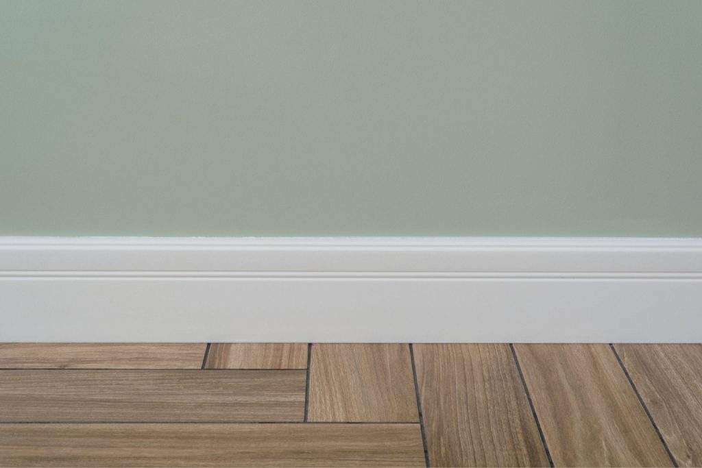  A white baseboard trim with a simple design covers the gap where the floor and the wall connect 