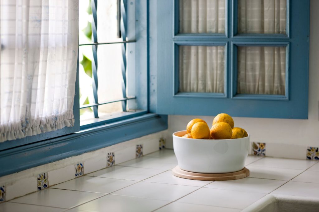 A kitchen corner with blue windows and a bowl of fruit placed on top of a tiled countertop
