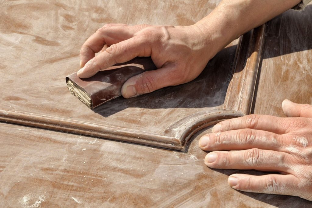 A person manually sanding a wooden door to remove its old varnish