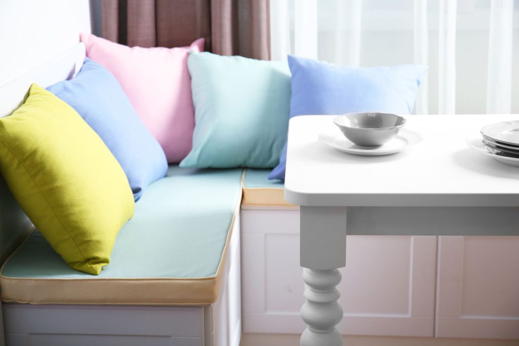 A kitchen bay window with colourful pillows and a small dining table 