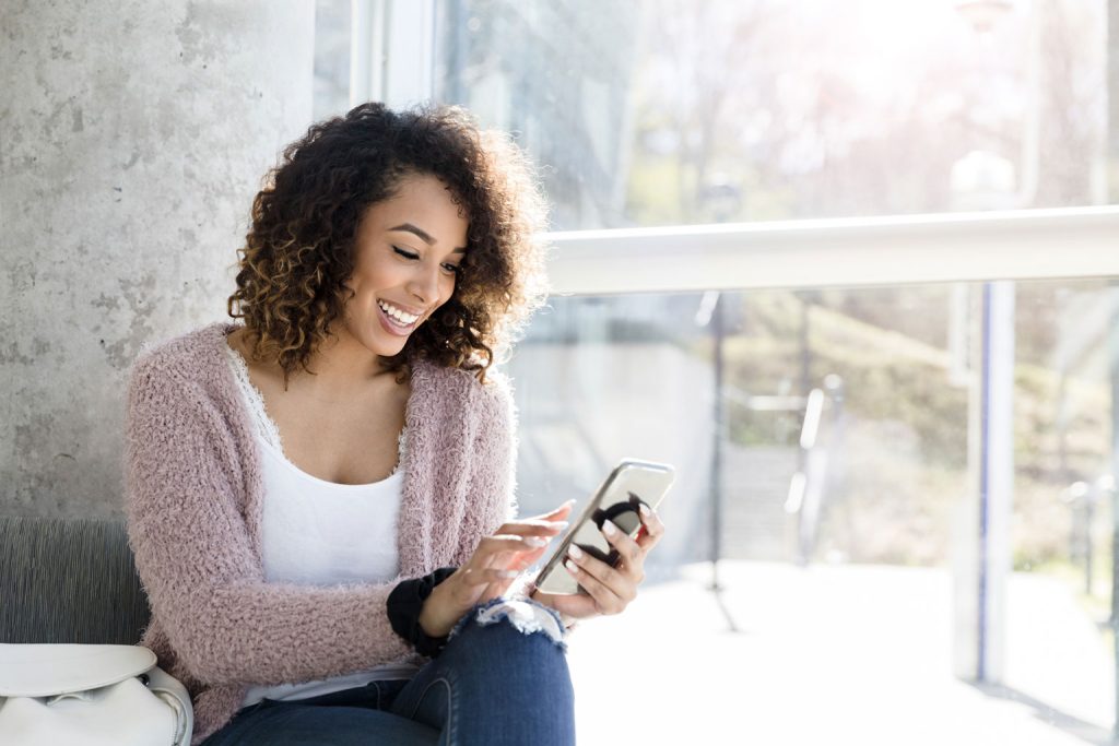 Person smiling while using their phone by the window 