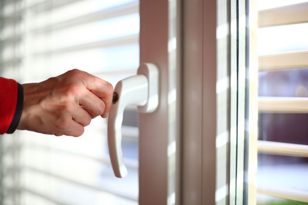 A person locking a casement window with a keyed lock