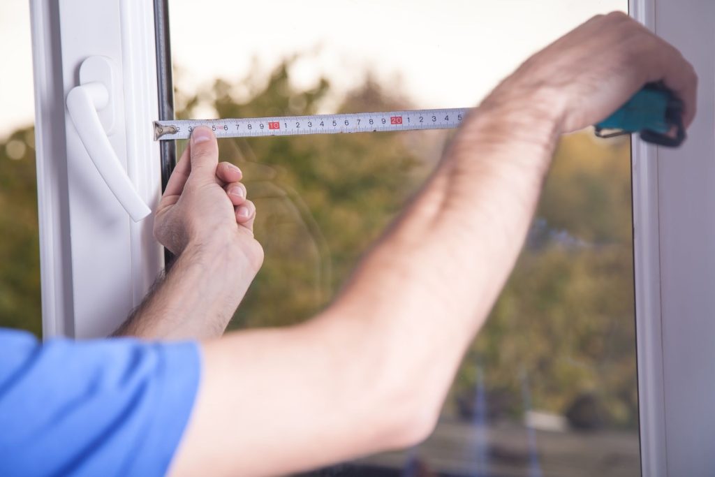 A person holds an extended tape measure against a window pane