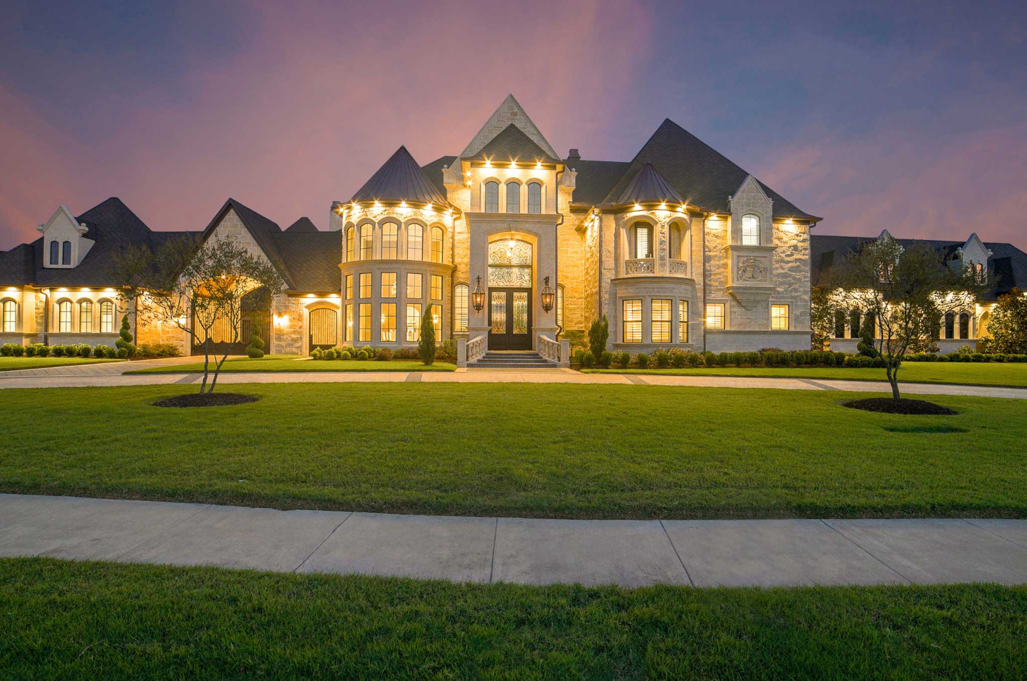 The front yard of a lit mansion at dusk