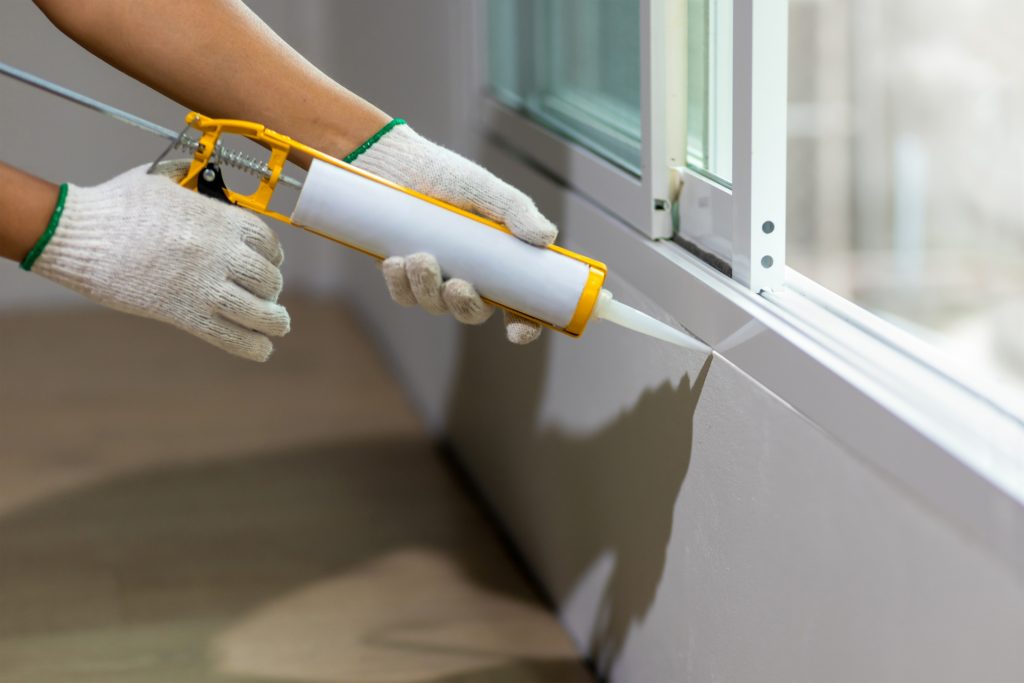 An Ontario homeowner wearing gloves caulking their windows as a regular part of window maintenance. 
