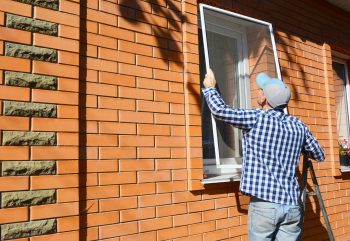 A worker installing a mesh wire screen over a window