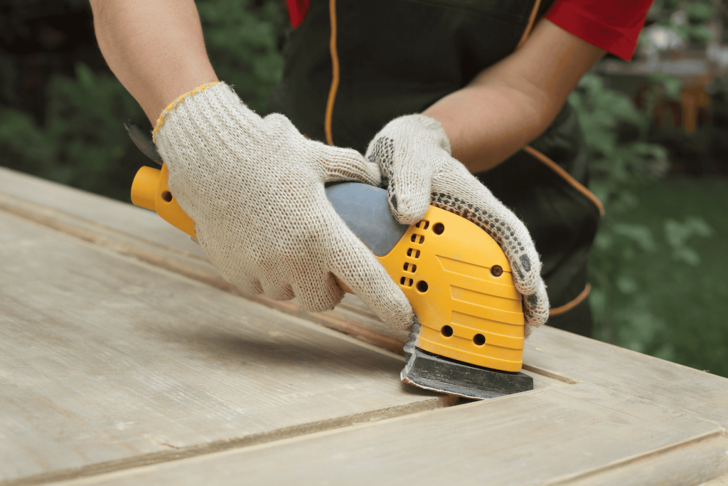 A worker sanding a wooden door panel with a power tool