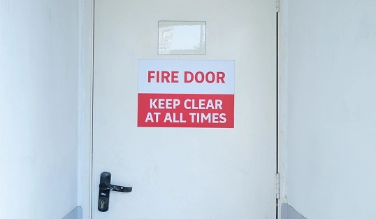 A fire-rated door with a sign that says “Fire Door, Keep Clear at All Times”