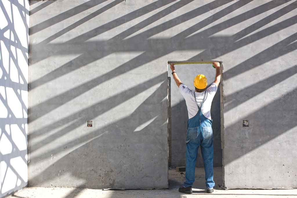 Construction worker wearing a hard hat, measuring the top of a door frame 